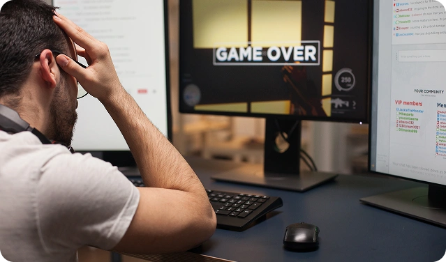 Egy gamer csalódottan ül a számítógép előtt miközben a monitoron a Game Over felirat látható