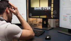 Egy gamer csalódottan ül a számítógép előtt miközben a monitoron a Game Over felirat látható